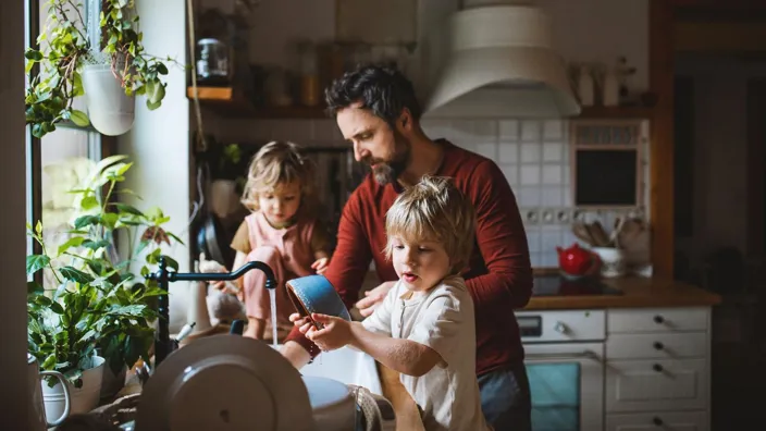 Mature father with two small children washing dishes indoors at home, daily chores concept.