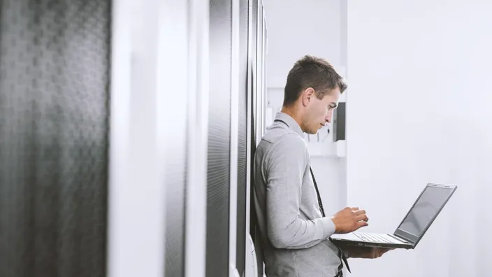 Portrait of modern young man holding laptop standing in server room working with supercomputer