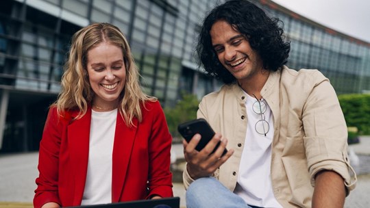 Man and woman working on laptop using cell phone smiling next to Tietoevry office building