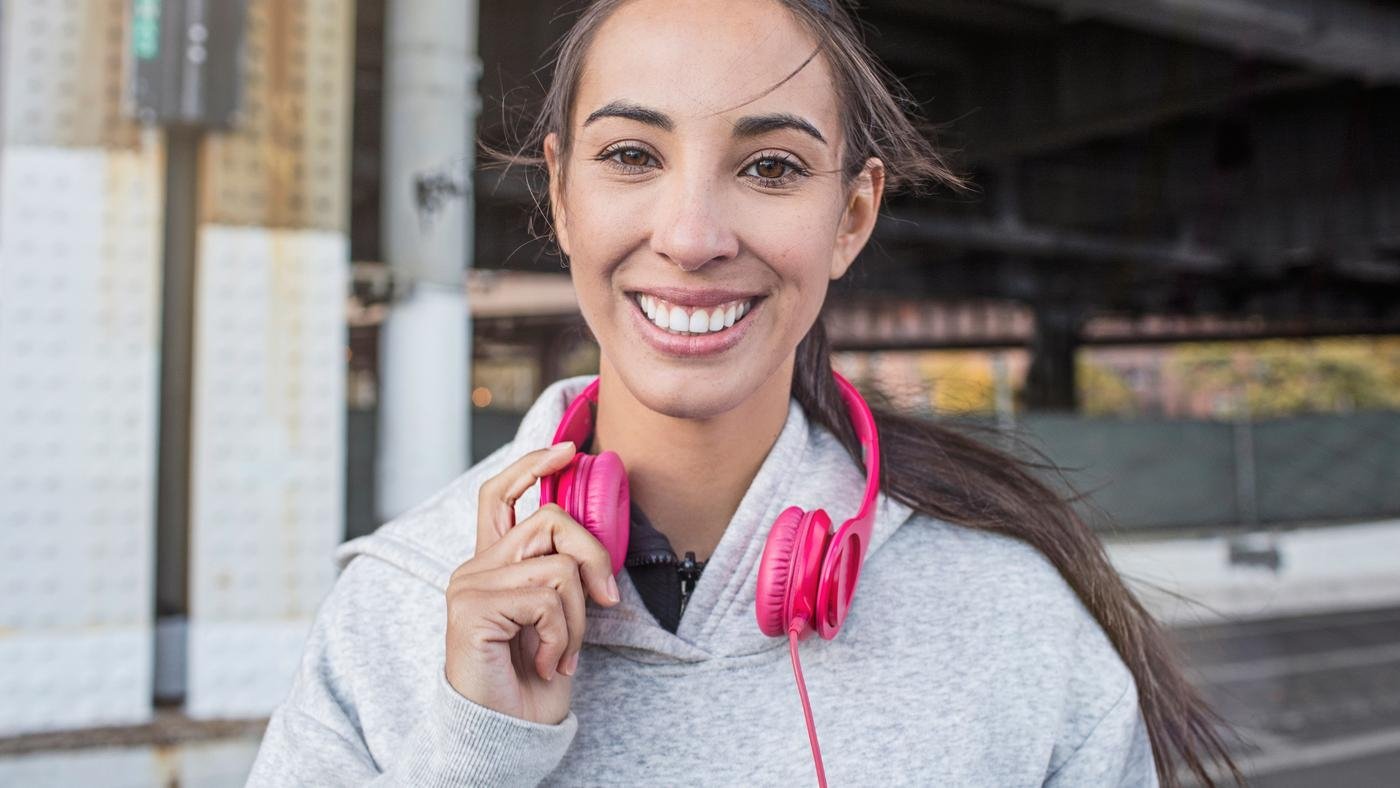 Portrait of smiling young athlete with headphones. Confident fit woman is wearing sportswear.