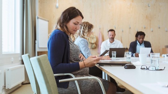 Pregnant woman uses mobile phone during meeting with colleagues